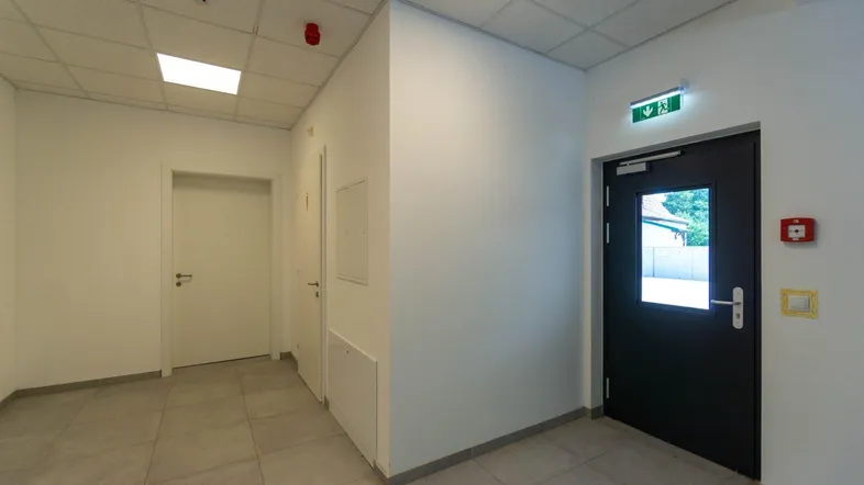 Heller Flur mit Fliesenboden, weißen Wänden und einer Sicherheitstür zum Ausgang.