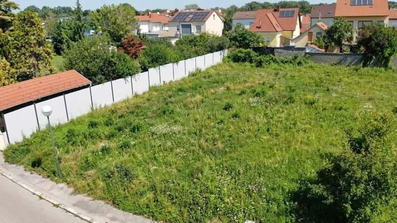 Luftaufnahme eines unbebauten Grundstücks mit Grasfläche, umgeben von Wohnhäusern und einem Zaun.