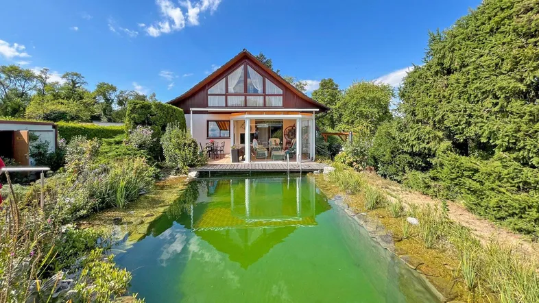 Haus mit großem Naturschwimmteich und Wintergarten in idyllischer grüner Umgebung.