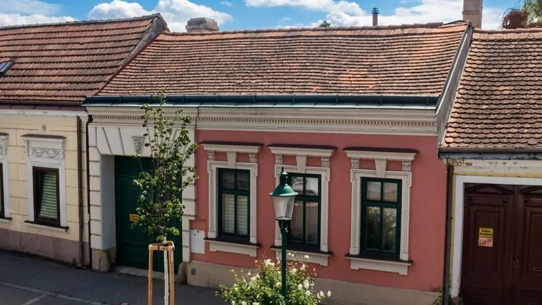 Rosa Hausfassade mit grünen Fenstern und traditioneller Architektur unter blauem Himmel.