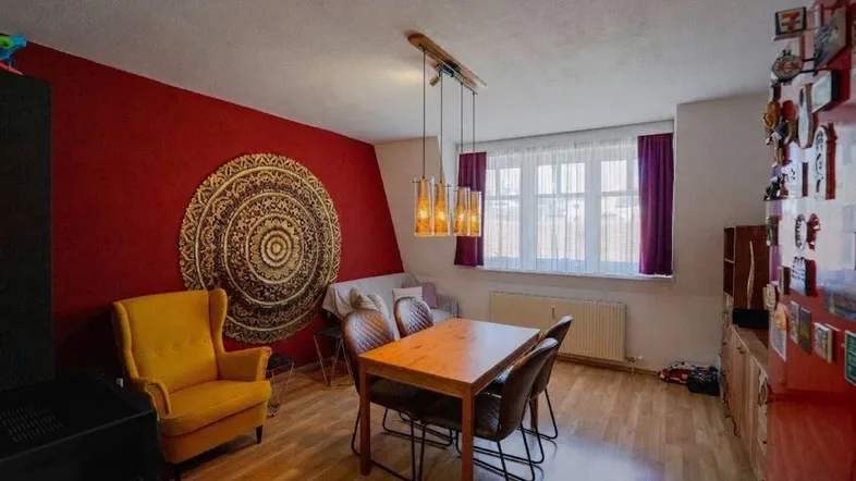 Geräumiger Wohn-Essbereich mit Holzboden, roter Akzentwand und großem Fenster.