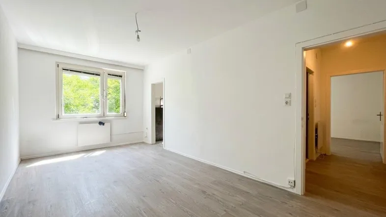 Helles, unfurniertes Zimmer mit Laminatboden und Fensterblick ins Grüne.