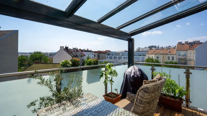 Überdachter Balkon mit Sitzgelegenheiten, Pflanzen und weitem Blick über die Stadt.