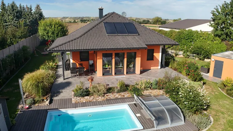 Luftaufnahme eines Einfamilienhauses mit Pool, Terrasse und gepflegtem Garten unter blauem Himmel.
