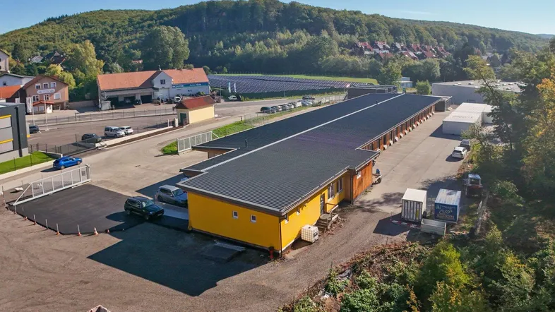 Luftaufnahme des Gewerbeobjekts mit langem Gebäude, Parkplätzen und umgebender grüner Landschaft.