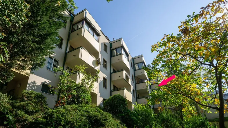 Mehrfamilienhaus mit Balkonen und üppiger Begrünung unter blauem Himmel.