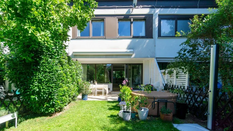 Sonniger Gartenbereich mit gepflegtem Rasen, Terrasse, Whirlpool und Außendusche, ideal für Entspannung im Freien.