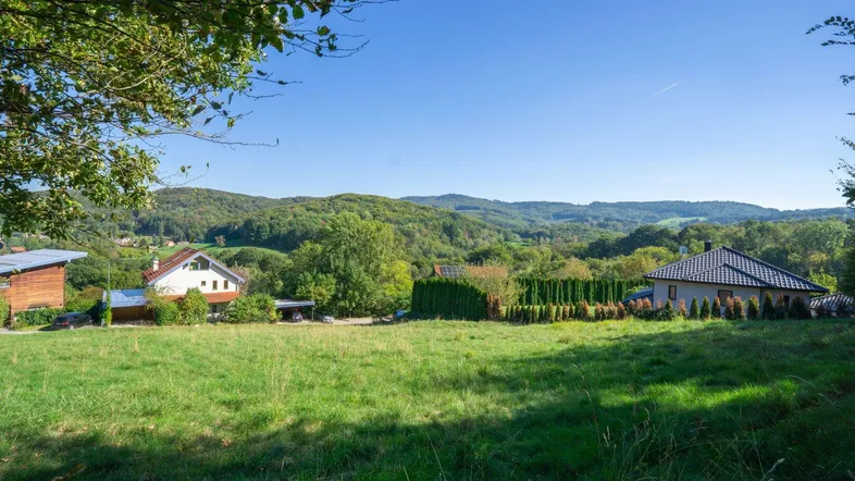 Weitläufige Landschaft mit grünen Hügeln und vereinzelten Wohnhäusern unter blauem Himmel.