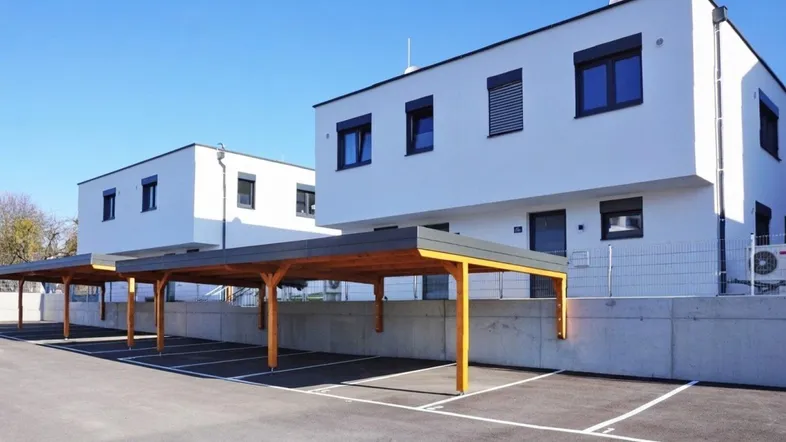 Moderne weiße Gebäude mit Flachdach und überdachten Parkplätzen unter Holzcarports.