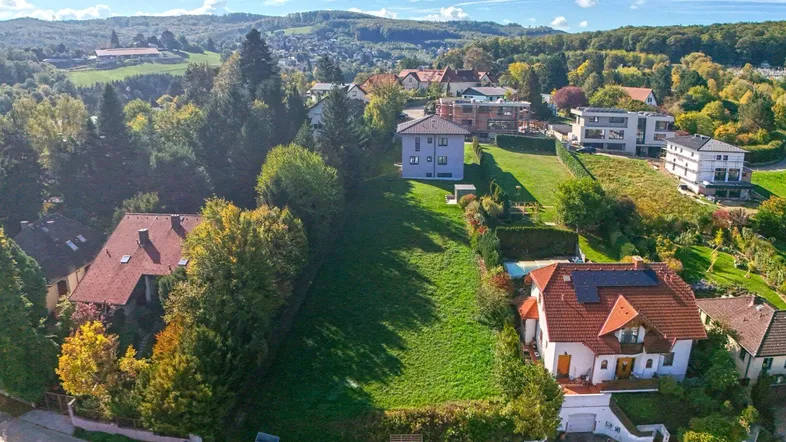 Luftaufnahme eines großen grünen Grundstücks mit umliegenden Häusern und bewaldeten Hügeln im Hintergrund.