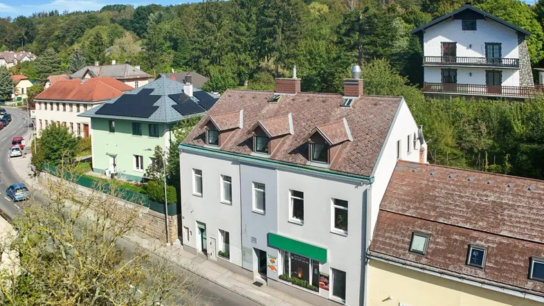 Luftaufnahme eines Mehrfamilienhauses mit Geschäften im Erdgeschoss und umliegender grüner Landschaft.