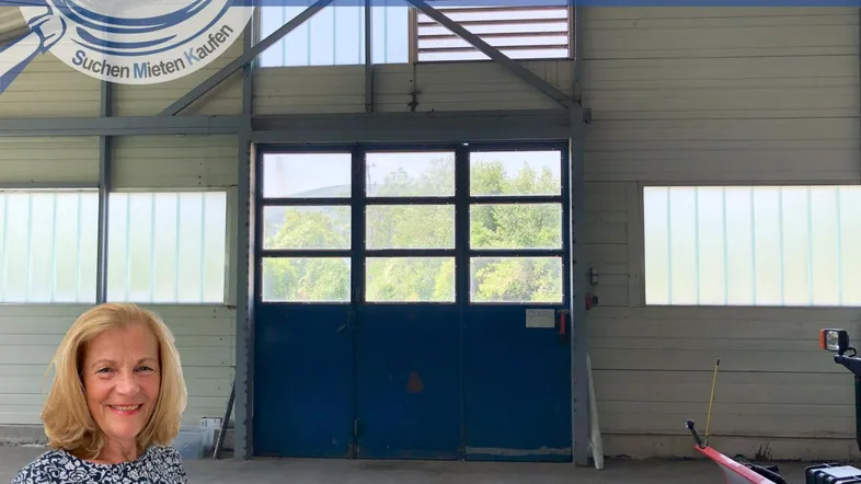 Innenansicht einer Lagerhalle oder Werkstatt mit großem Tor und Fenstern, gut beleuchtet.