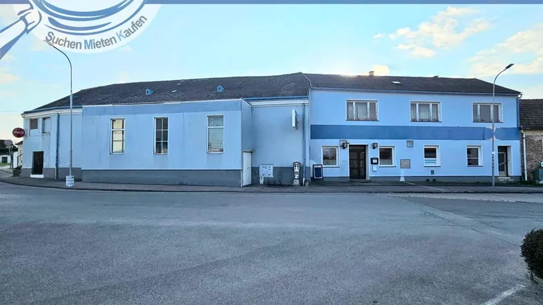 Blau gestrichenes Gebäude an einer Straßenecke mit mehreren Fenstern und einem Werbebanner.