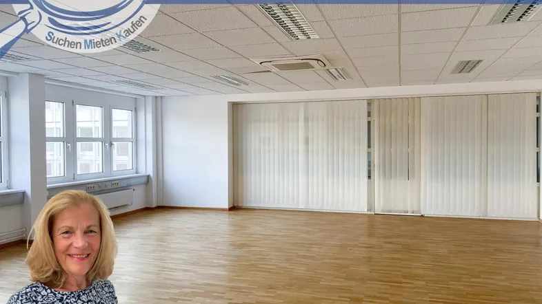 Heller, leerer Büroraum mit großen Fenstern, Holzfußboden und Deckenbeleuchtung.