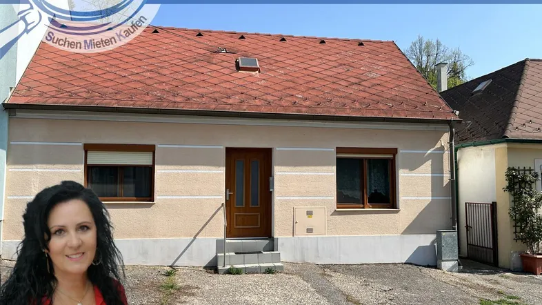 Einfamilienhaus mit Putzfassade und Ziegeldach, umgeben von einer kleinen Grünfläche.