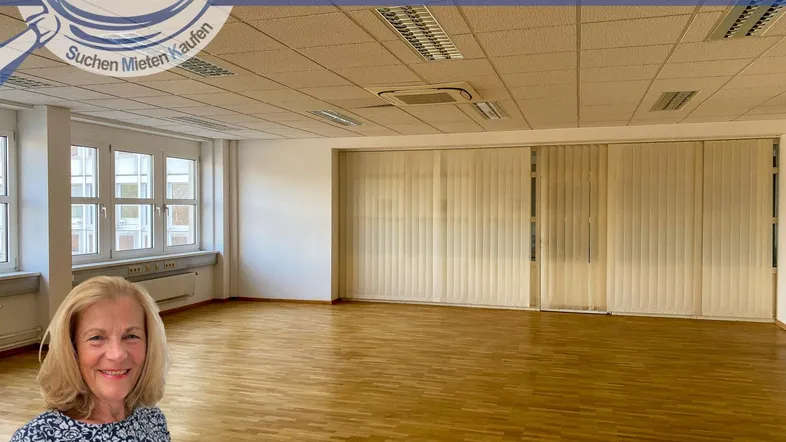 Geräumiges, leeres Büro mit großen Fenstern, Holzfußboden und einer Decke mit integrierter Beleuchtung.