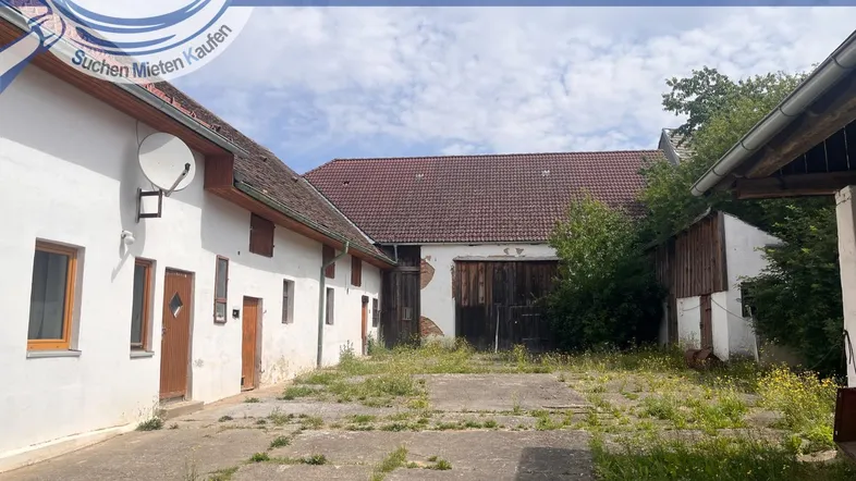 Altes Bauernhaus mit großem Innenhof und Nebengebäuden unter bewölktem Himmel.