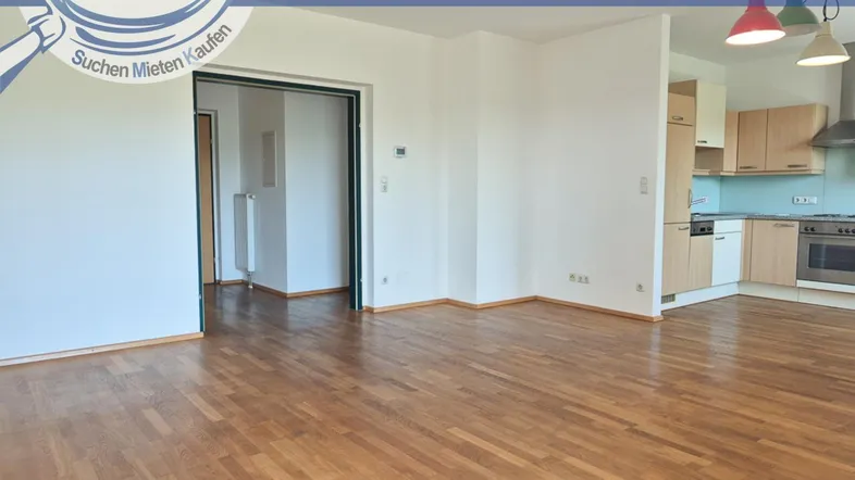 Geräumiges Wohnzimmer mit Parkettboden und offener Verbindung zu einer modernen Küche.