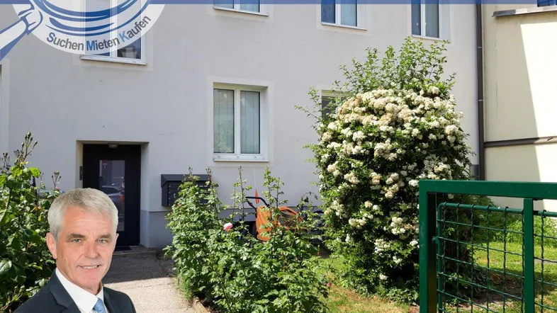 Eingangsbereich eines Mehrfamilienhauses mit gepflegter Grünfläche und blühenden Sträuchern.