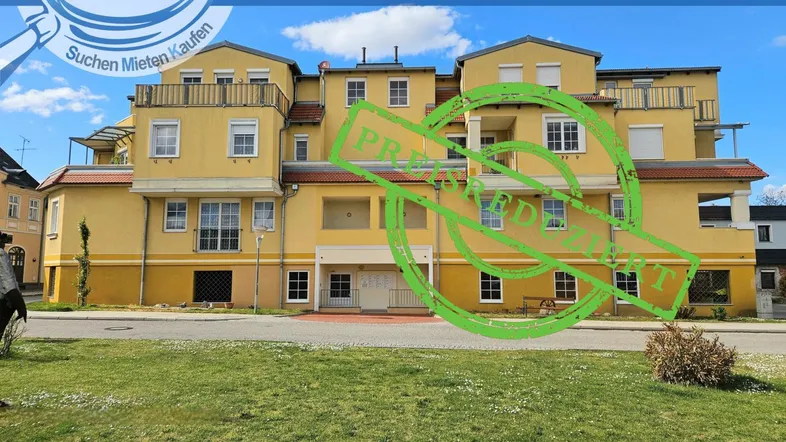 Gelbes Mehrfamilienhaus mit mehreren Balkonen und grüner Rasenfläche davor unter blauem Himmel.