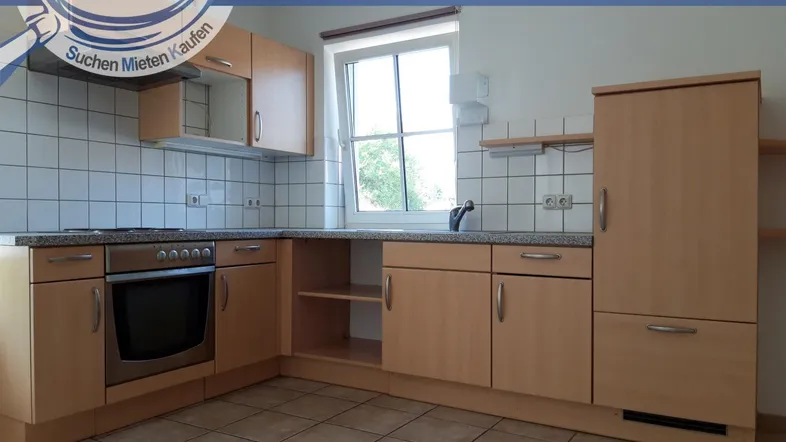 Helle Einbauküche mit Holzfronten, Fliesenboden und einem Fenster mit Blick ins Grüne.