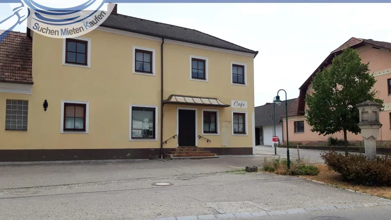 Gelbes Gebäude mit Café im Erdgeschoss und weiteren Fenstern, an einer Straße gelegen.
