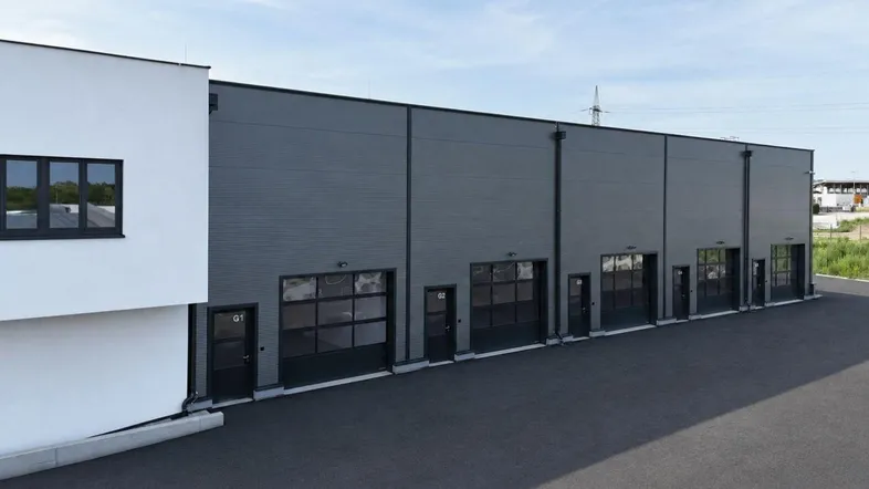Moderne Gewerbehalle mit mehreren Rolltoren und weißer Fassade unter blauem Himmel.