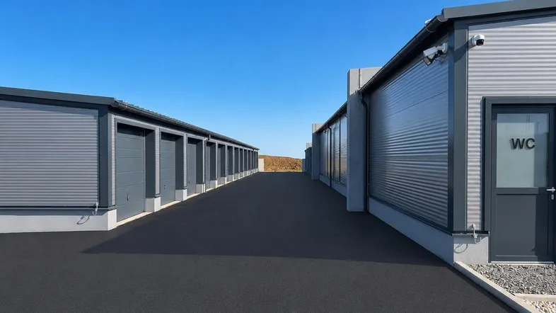Moderne Lagerhallen und Garagen mit asphaltierter Zufahrt und klarem blauen Himmel.