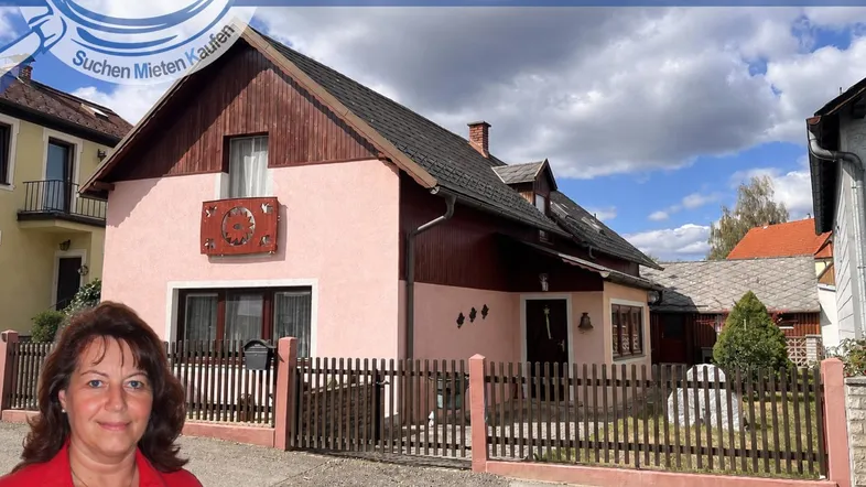 Rosa gestrichenes Einfamilienhaus mit braunem Dach und Holzelementen unter bewölktem Himmel.