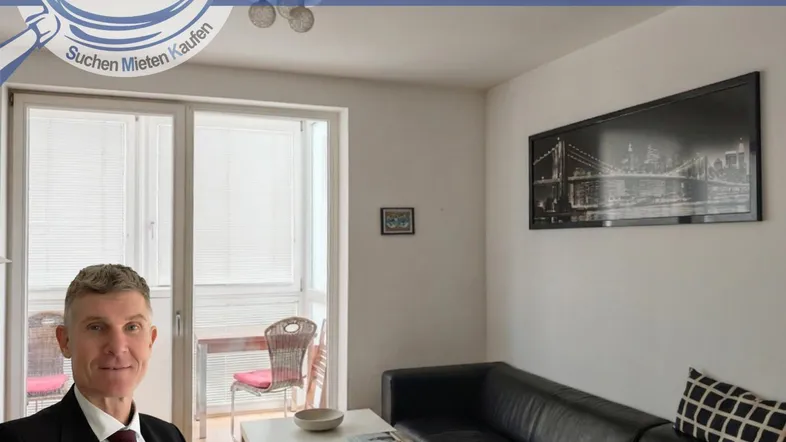 Helles Wohnzimmer mit schwarzem Sofa, Couchtisch und Zugang zu einem Balkon oder einer Loggia.