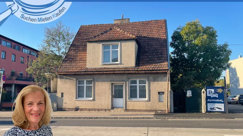 Altes Einfamilienhaus an einer Straße mit sichtbarem Renovierungsbedarf und einer Maklerin im Vordergrund.