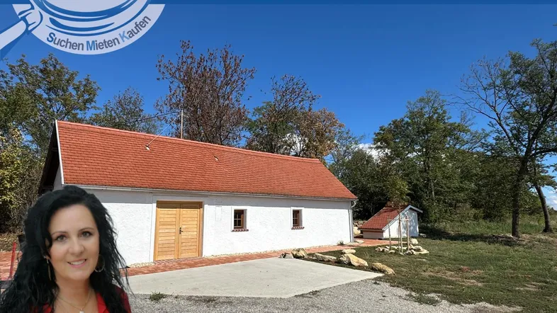 Weißes Gebäude mit rotem Dach in ländlicher Umgebung unter blauem Himmel.