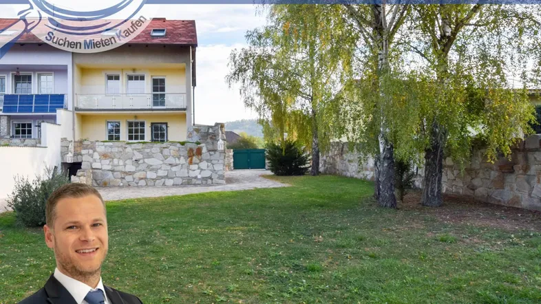 Vorderansicht des Hauses mit gepflegtem Rasen und Steinmauer, umgeben von Bäumen.