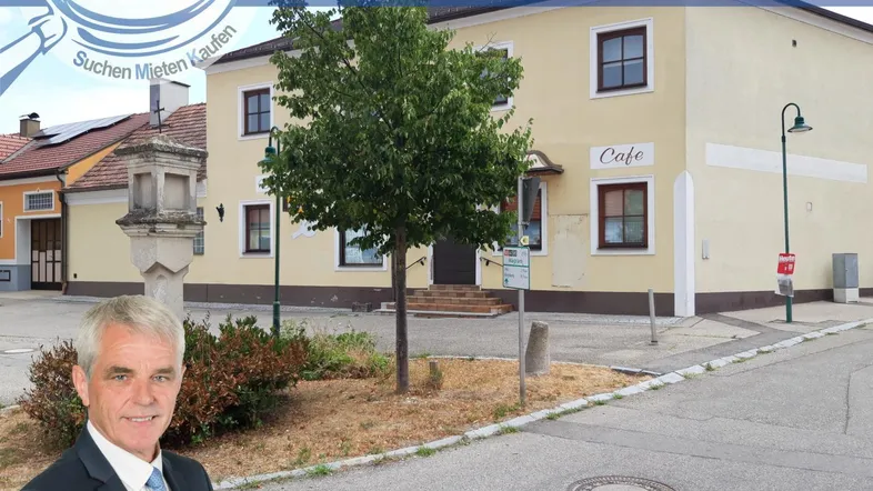 Gelbes Gebäude mit Café-Schild an einer Straße, umgeben von Bäumen und einem Denkmal.