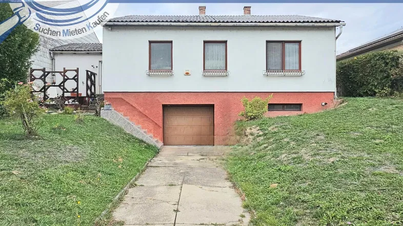 Vorderansicht eines Einfamilienhauses mit integrierter Garage und Zufahrt im Grünen.