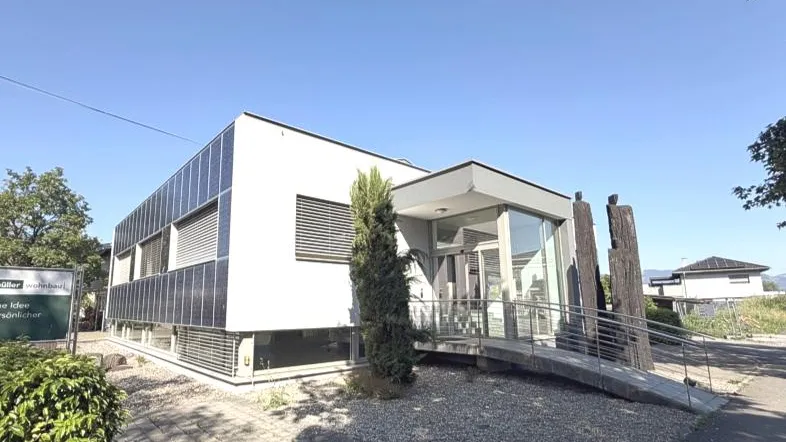 Modernes Bürogebäude mit großen Fenstern, Photovoltaikanlage und barrierefreiem Zugang über eine Rampe.