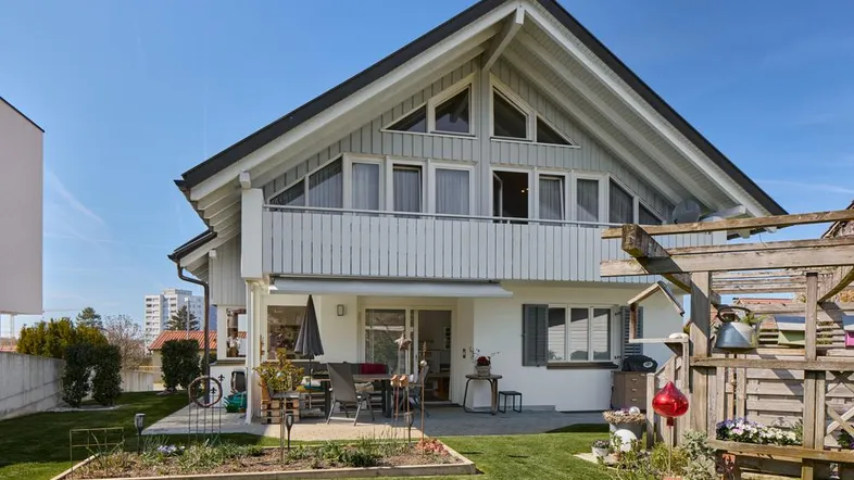 Charmantes Einfamilienhaus mit großer Terrasse, Garten und Balkon unter blauem Himmel.