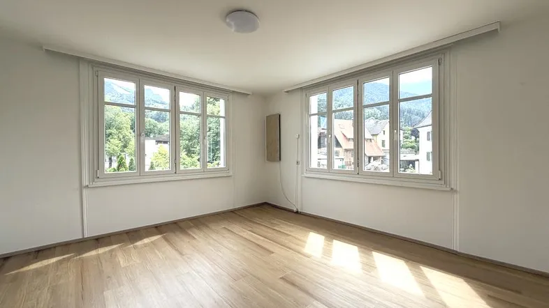 Helles Zimmer mit Holzboden und weissen Wänden, bietet einen schönen Blick ins Grüne.