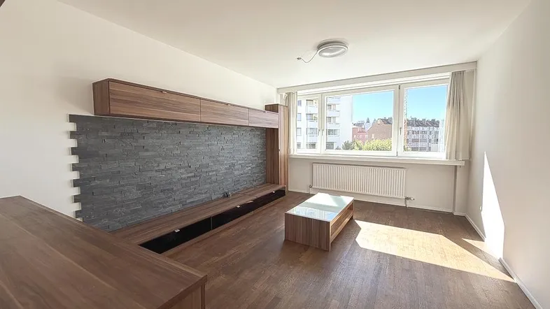 Helles Wohnzimmer mit Holzboden, moderner Wohnwand und großem Fenster mit Stadtblick.