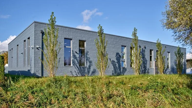 Modernes Geschäftsgebäude mit grauer Fassade und hohen Fenstern unter blauem Himmel.