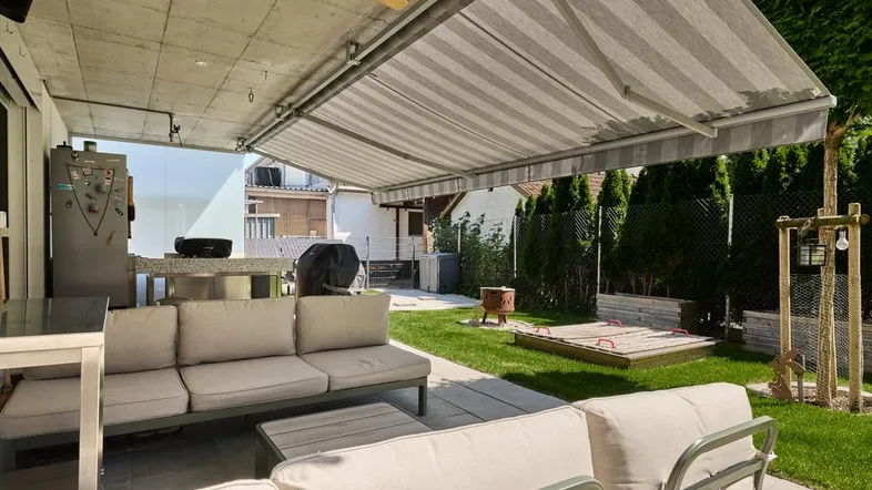 Geräumige Terrasse mit bequemen Gartenmöbeln, Markise und Zugang zum grünen Garten mit Sandkasten.