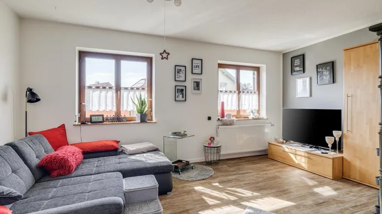 Helles Wohnzimmer mit grauem Ecksofa, Holzboden und zwei Fenstern.