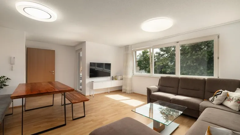 Helles Wohn- und Esszimmer mit Holzboden, großem Fenster und bequemer Sofalandschaft.