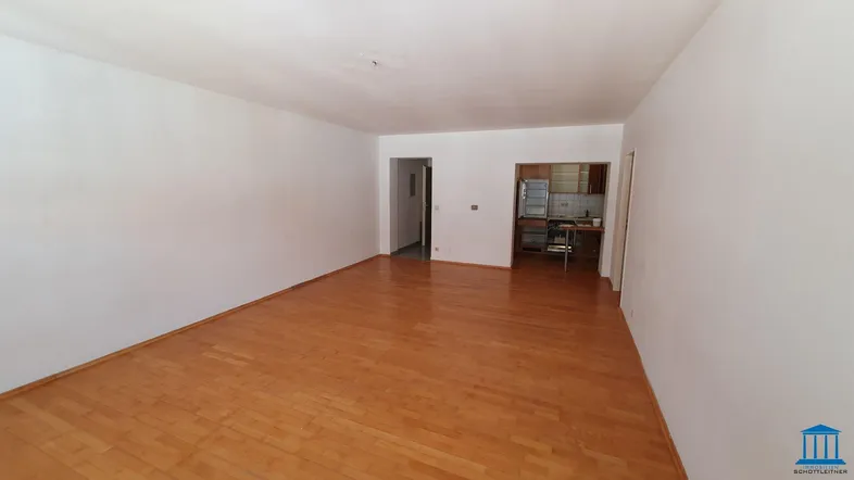 Geräumiges Wohnzimmer mit hellem Parkettboden und offenem Zugang zu einer separaten Küche.