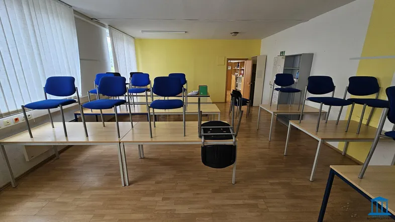 Geräumiger Konferenzraum mit mehreren Tischen und blauen Stühlen, ideal für Schulungen oder Besprechungen.