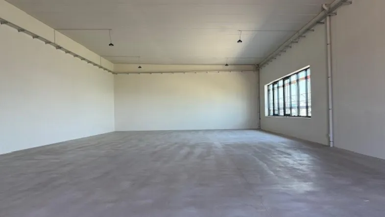 Großer, leerer Raum mit Betonboden und Fenstern, ideal für Lager oder Werkstatt.