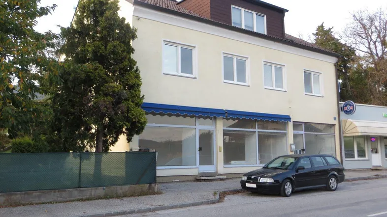 Ansicht des Gebäudes von der Straße mit einer blauen Markise und einem geparkten Auto davor.