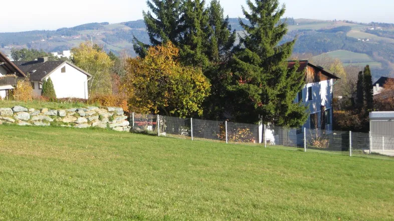 Weitläufige Grünfläche mit Blick auf umliegende Häuser und bewaldete Hügel in der Ferne.