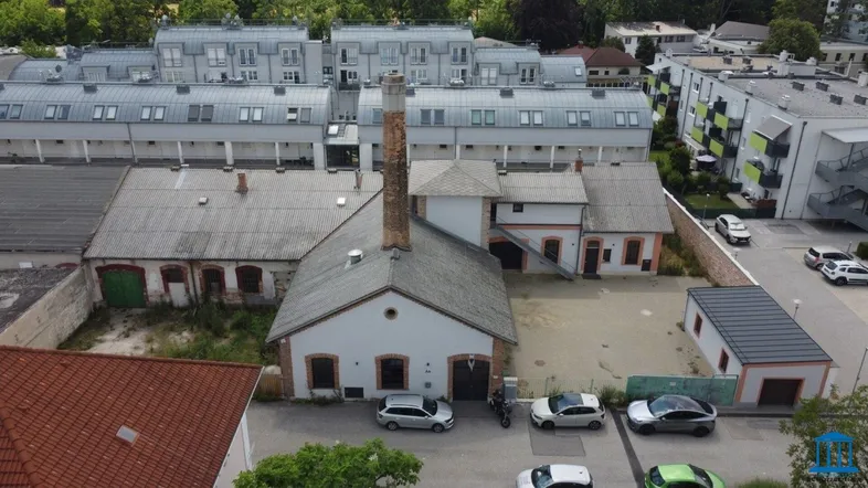 Luftaufnahme eines historischen Industriegebäudes mit Schornstein, umgeben von modernen Wohngebäuden und Parkplätzen.