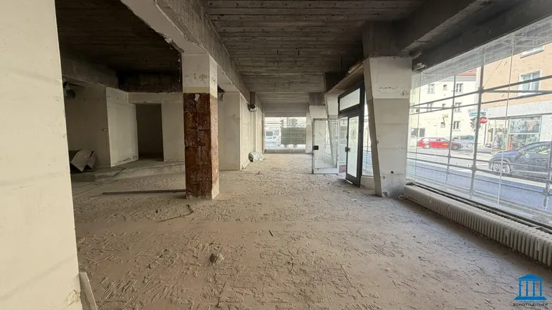 Geräumiges Ladenlokal im Rohbau mit Betonboden, tragenden Säulen und großen Fenstern zur Straßenseite.